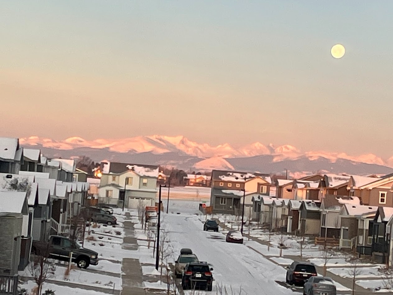 Winter neighborhood street with snowy mountain range and moon overhead